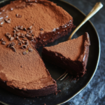 A slice of rich chocolate torte topped with powdered sugar and served with fresh berries.